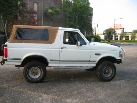 1992 Ford Bronco - Side profile of a white 1992 Ford Bronco a tan soft top and aftermarket wheels.
