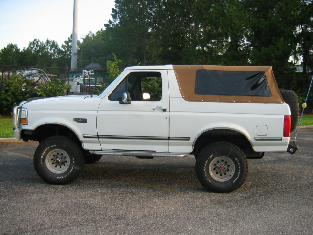 White Ford Bronco with tan soft top, lifted on off-road tires, side view in a parking lot