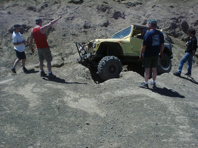 Yellow Jeep Wrangler with large tires navigating rocky terrain, people watching