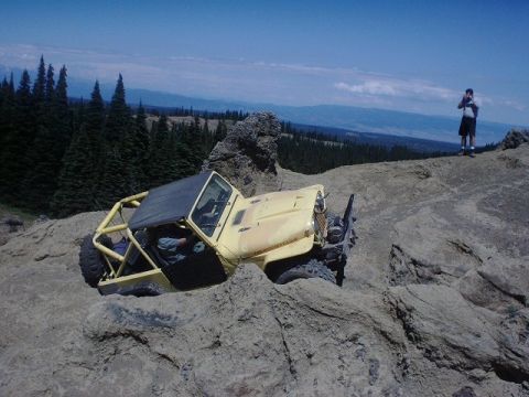 1978 Ford Bronco - A yellow off-road vehicle navigates a steep, rocky incline under a clear blue sky.