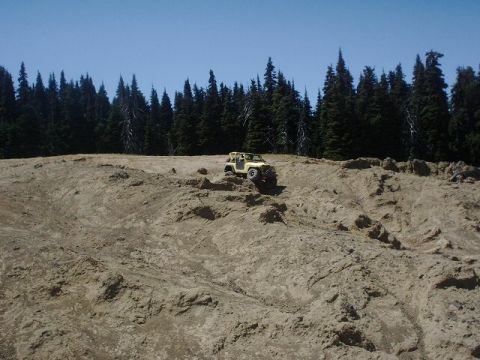 1978 Ford Bronco - Off-road vehicle navigates a steep dirt incline under a clear blue sky.