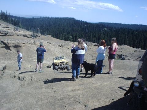 1978 Ford Bronco - A group of people and a dog observe a yellow off-road vehicle on a rocky, elevated terrain.