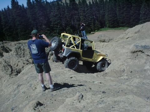 1978 Ford Bronco - A yellow off-road vehicle navigates a steep, rocky incline with a person photographing it.