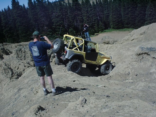 Yellow off-road vehicle with roll cage on rocky terrain, driver visible inside