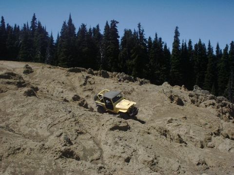 1978 Ford Bronco - This yellow off-road vehicle navigates a challenging rocky landscape, with a dense forest visible behind it.