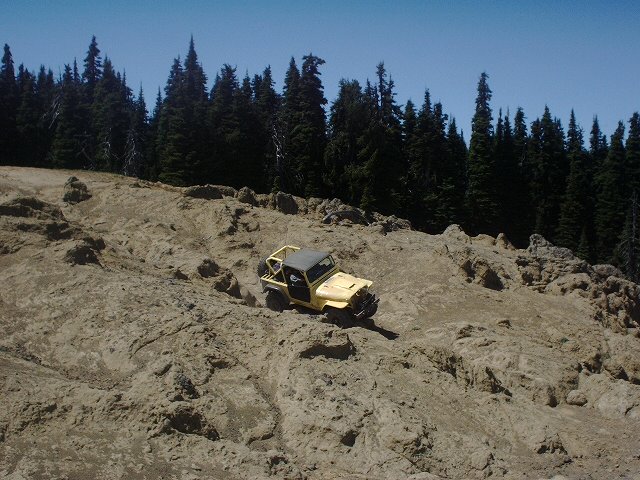 Yellow off-road vehicle on rocky terrain with trees in background