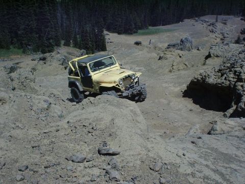 1978 Ford Bronco - Jeep CJ-7 tackling a challenging off-road course in a mountainous, wooded area.