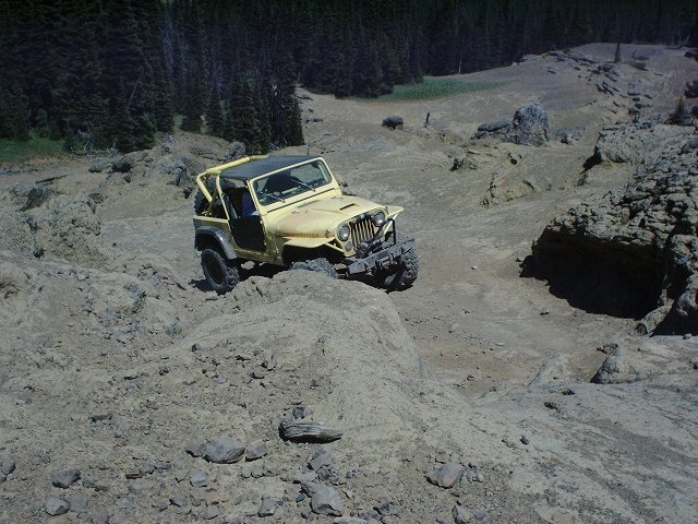 Yellow Jeep CJ-7 navigating a steep, rocky trail with trees in the background
