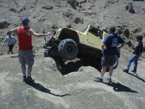 1978 Ford Bronco - Off-road enthusiasts observe a yellow vehicle navigating a challenging rocky course.