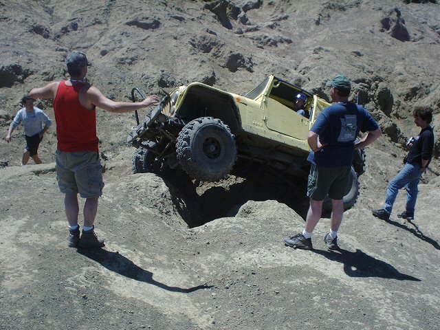 Yellow off-road vehicle tilted on rocky terrain with people watching