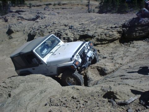 1978 Ford Bronco - White Jeep Wrangler tackling a challenging rocky off-road course.