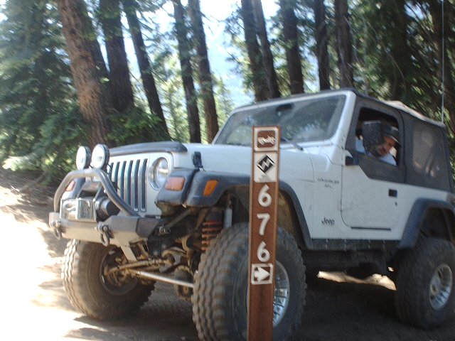 White Jeep Wrangler with off-road tires and bumper parked on a dirt trail