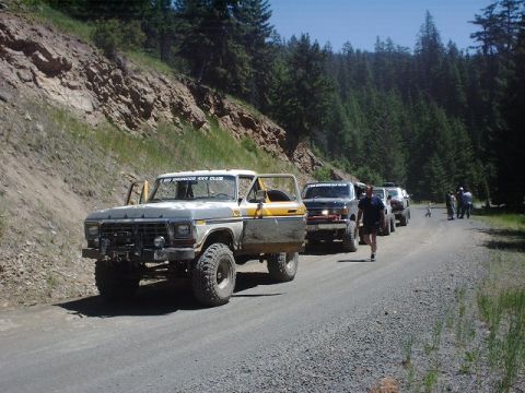 1978 Ford Bronco - A line of off-road vehicles, including a 1978 Ford Bronco, travels down a dusty mountain road.