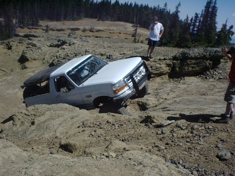1978 Ford Bronco - A white Ford Bronco is stuck in a challenging off-road terrain, with onlookers observing the situation.