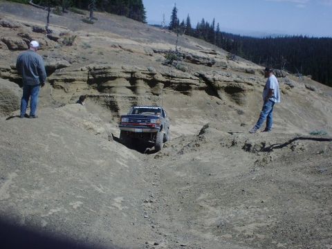 1978 Ford Bronco - A dark pickup truck tackles a challenging off-road course on a sunny day.