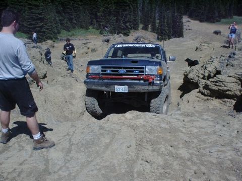 1978 Ford Bronco - A dark blue Ford Bronco tackles a challenging off-road course with spectators present.