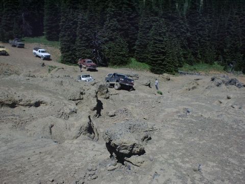 1978 Ford Bronco - Several off-road vehicles traverse a challenging, rocky terrain under a dense forest canopy.
