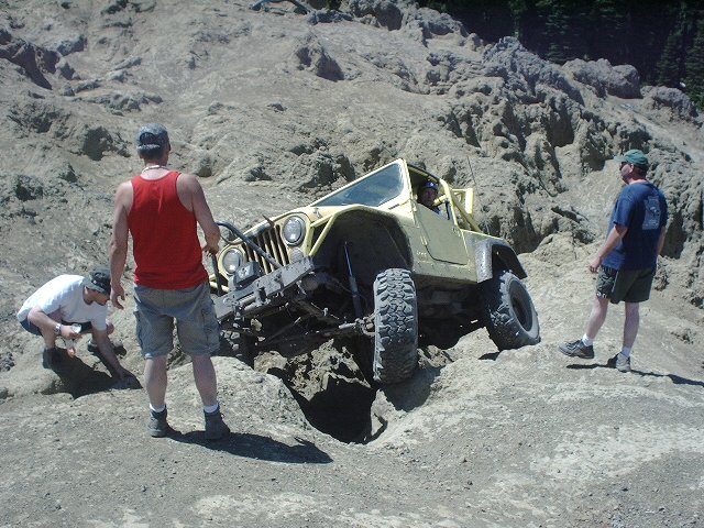 Yellow Jeep Wrangler off-roading on a steep, rocky incline with people watching