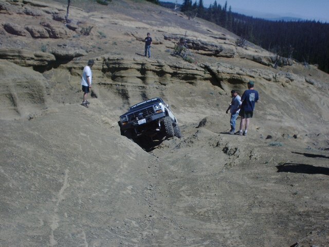 White SUV with off-road tires climbing a steep dirt incline