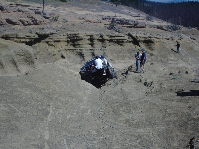 Off-road vehicle on a steep dirt slope with people watching
