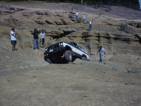 1978 Ford Bronco - A white 1978 Ford Bronco is stuck on a steep, sandy incline while onlookers observe the off-road situation.