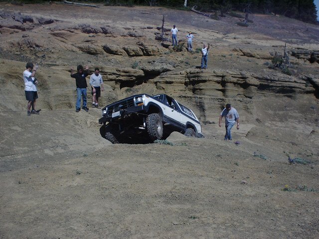 White 1978 Ford Bronco stuck on a dirt hill with people watching