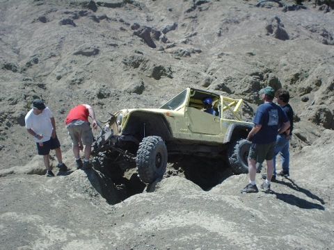 1978 Ford Bronco - Off-road Jeep Wrangler with roll cage navigating difficult terrain with assistance from onlookers.