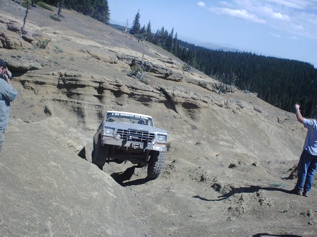 1978 Ford Bronco climbing a steep, rocky hill with two people watching