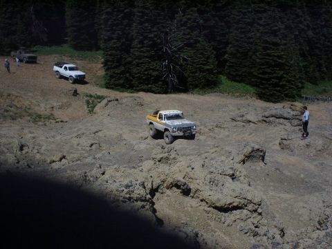 1978 Ford Bronco - Several off-road vehicles navigate a rocky landscape with trees in the background.