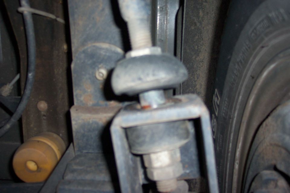 Undercarriage bolt, bracket and rubber bushing near a tire, dusty and lightly rusted