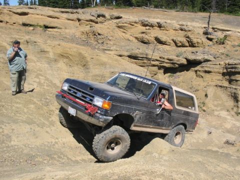 1995 Ford Bronco - A man stands on a dirt embankment watching a Ford Bronco navigate a steep, sandy incline.