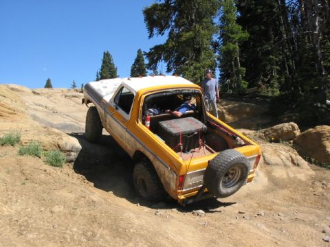 1995 Ford Bronco - A yellow and white Ford Bronco navigates a challenging rocky terrain under a clear blue sky.
