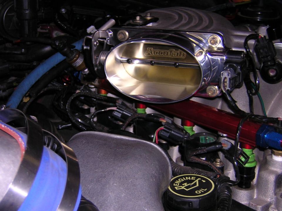 Close-up of a shiny Accufab throttle body and green fuel injectors in an engine bay