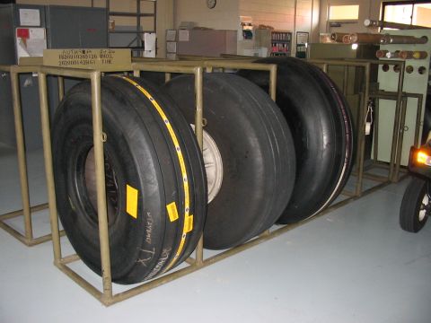 1988 Ford Bronco - Several large tires are stored on a metal rack in what appears to be a warehouse or garage setting.