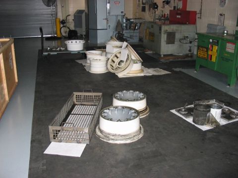 1988 Ford Bronco - Various wheels and automotive parts are laid out on the floor of a workshop, with machinery visible in the background.