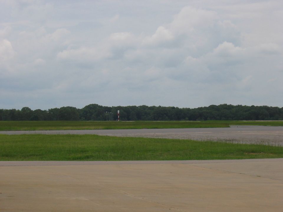 Airport runway with grass and trees in the background under a cloudy sky. Supermotors logo in the corner