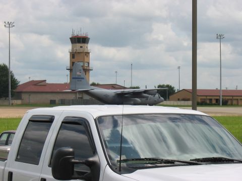 1988 Ford Bronco - A white pickup truck is parked in front of an airport scene with a C-130 aircraft and control tower.