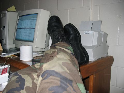 1988 Ford Bronco - A person's feet in camouflage pants and black boots are resting on a desk in front of a computer monitor and a printer.