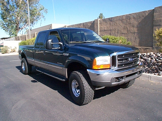 Dark green Ford F-series Super Duty crew cab with long bed lifted on chrome wheels in a parking lot