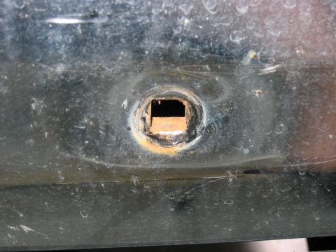1988 Ford Bronco - Detail of a rusted square opening on a dark vehicle component.