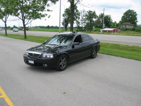 2000 Ford Crown Victoria - Three-quarter front view of a black Lincoln LS sedan with a chrome waterfall grille, tinted windows and dark five-spoke alloy wheels, parke…