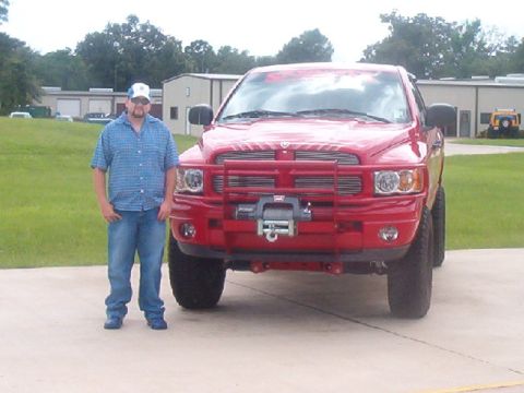 1980 Ford Bronco - A man poses with his red Dodge Ram pickup truck, which is equipped with a winch and brush guard.