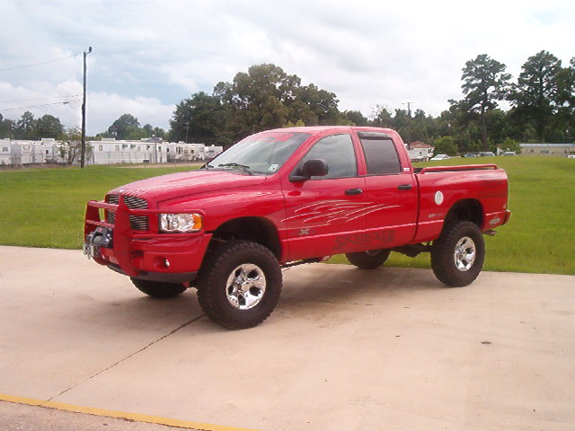 Red pickup truck with aftermarket bull bar and large tires, parked on concrete