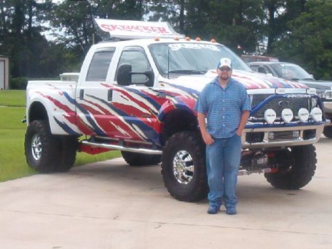 1980 Ford Bronco - A man poses with a heavily modified pickup truck custom paint and a roof-mounted sign.