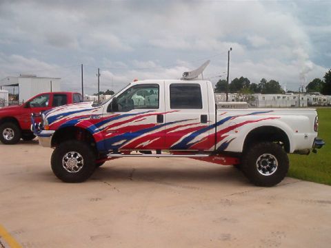 1980 Ford Bronco - Lifted pickup truck with patriotic graphics parked next to a red pickup truck under a cloudy sky.