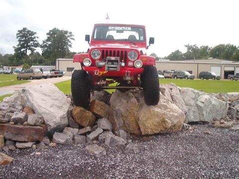 1980 Ford Bronco - A red Jeep Wrangler is positioned on a pile of large rocks, demonstrating its off-road capabilities.