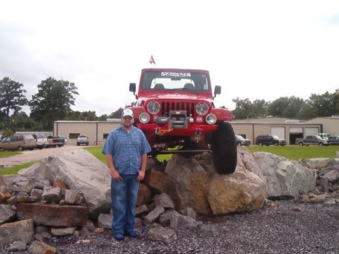 1980 Ford Bronco - Red lifted Jeep Wrangler perched nose-out atop a rock pile, showing its seven-slot grille, round driving lights, front winch and Skyjacker…