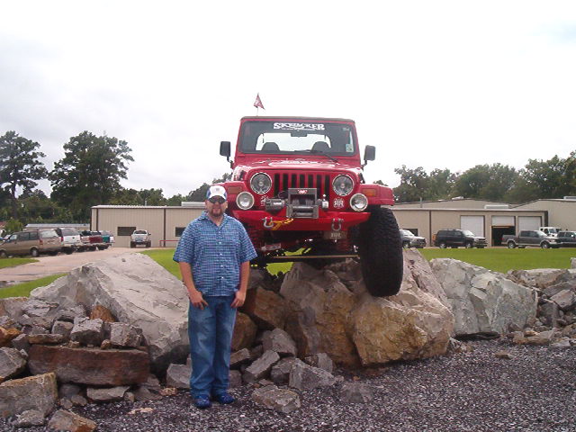 Red lifted Jeep Wrangler with winch atop a rock pile, man standing in front of it