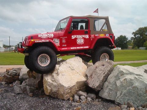 1980 Ford Bronco - Red Jeep Wrangler with a tan soft top posed climbing a pile of white boulders, flexing its lifted suspension with the front wheel up on roc…