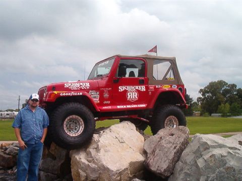 1980 Ford Bronco - A red Jeep Wrangler TJ show rig with a tan soft top perches on a pile of white limestone boulders under a cloudy sky, while a man in a blue…